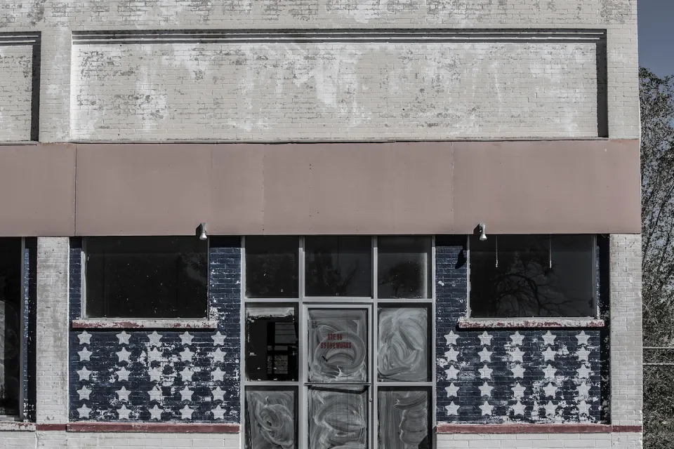 Faded image of vacant storefront in rural area with American flag stars painteind on windows.